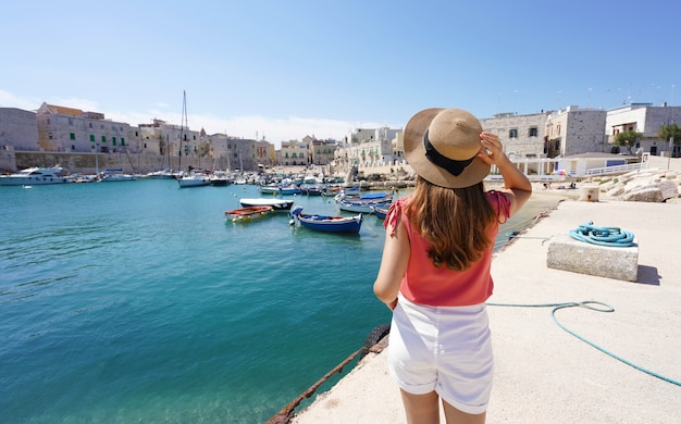 Visita l'Italia. Vista posteriore del giovane turista femminile che tiene il cappello e guarda il porto di Giovinazzo in Puglia, Italia.