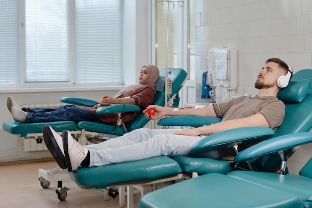 Visitatori di centri medici che donano sangue posando sulle sedie di procedura