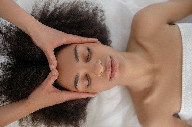 Viso, cosmetologia. Ragazza dai capelli scuri sdraiato sul divano con gli occhi chiusi e le mani di bellezza sulla fronte