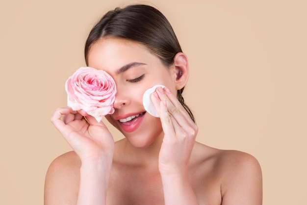 Viso di donna di bellezza con trucco naturale, fiori di rosa e con dischetti di cotone, spugna, batuffolo di cotone. Bellissimi cosmetici per il benessere femminile. Spa e benessere, concetto di cura della pelle. Trattamento facciale.