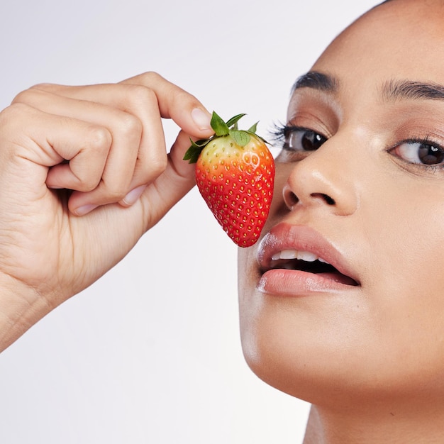 Viso labbra e fragola ritratto di una donna in studio per bellezza bagliore dermatologia o cosmetici naturali Persona di sesso femminile con frutta in mano per detox dieta sana e cura della pelle su sfondo bianco