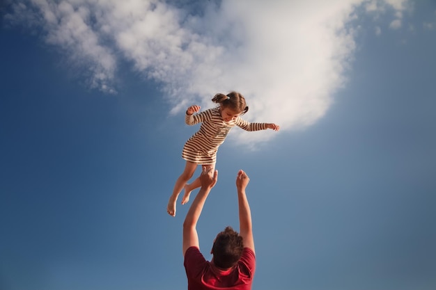 Vista a bassa angolazione del padre che lancia la figlia in aria contro il cielo