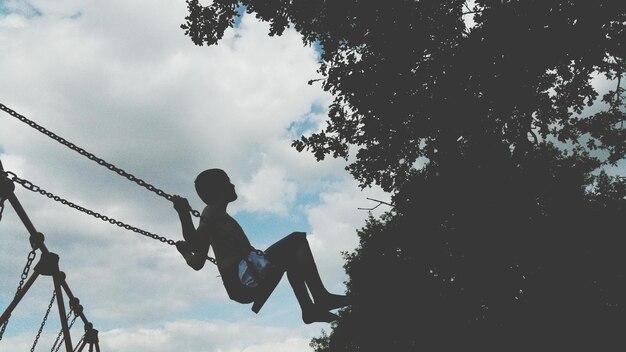 Vista a bassa angolazione di un ragazzo che gioca sull'altalena al parco contro il cielo