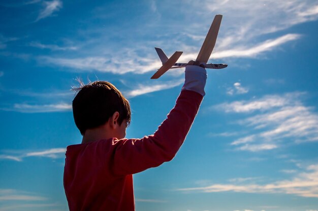 Vista a bassa angolazione di un ragazzo che tiene un modello di aereo contro il cielo blu