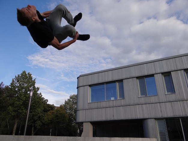 Vista a bassa angolazione di un uomo che esegue una acrobazia nel parco costruendo contro il cielo