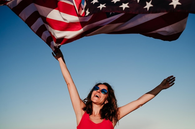 Vista a bassa angolazione di una donna con la bandiera americana contro un cielo blu chiaro