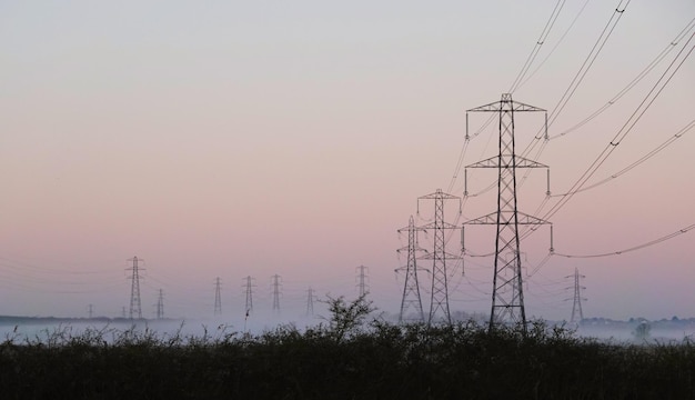 Vista a basso angolo dei pilastri elettrici sul campo contro il cielo durante l'alba