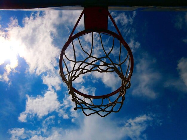 Vista a basso angolo del cerchio da basket contro il cielo nuvoloso durante una giornata di sole