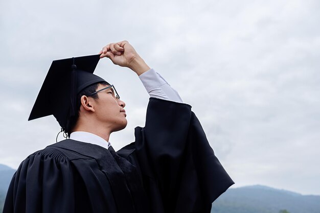 Vista a basso angolo di un giovane che indossa un abito da laurea in piedi contro il cielo