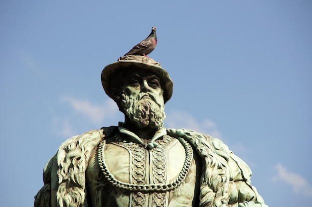 Vista a basso angolo di un piccione appoggiato a una statua maschile contro il cielo blu