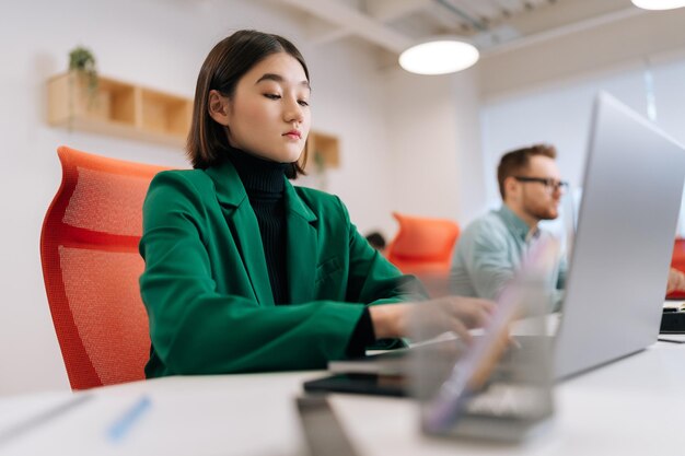 Vista a basso angolo di una programmatrice seria che scrive il codice del programma sulla tastiera del portatile in coworking