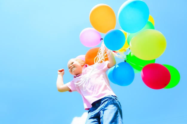 Vista a basso angolo di una ragazza con palloncini multicolori contro il cielo blu