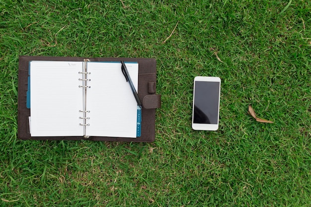 Vista ad alta angolazione del libro con telefono cellulare su un campo erboso
