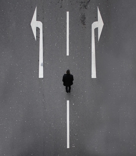 Vista ad alta angolazione dell'uomo in piedi dai simboli a freccia sulla strada