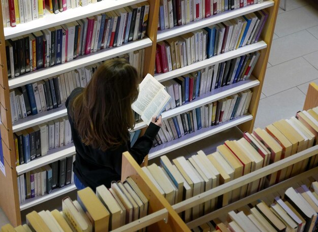 Vista ad alta angolazione di una donna che legge un libro sullo scaffale della biblioteca