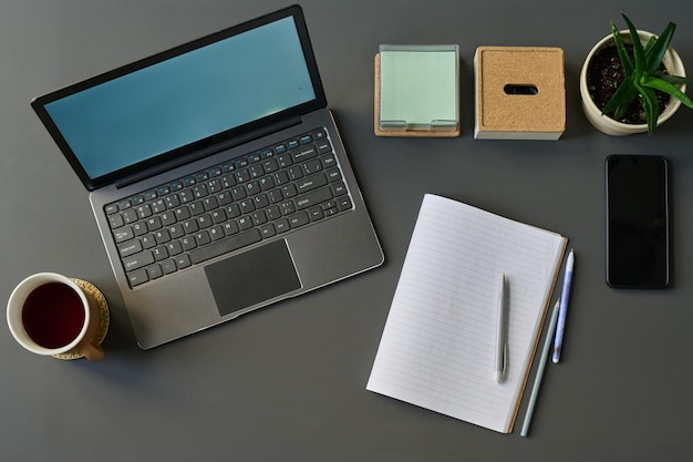 Vista ad alto angolo del blocco note del laptop per appunti e tazza di tè in piedi sul tavolo