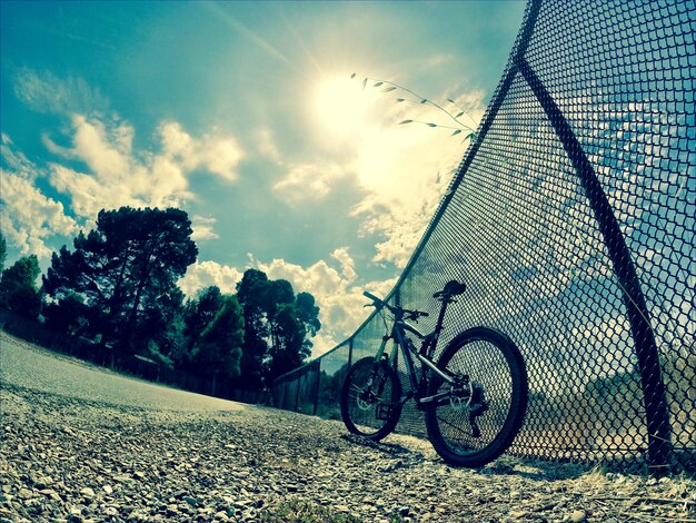 Vista ad alto angolo della bicicletta da una recinzione a catena sul campo contro il cielo