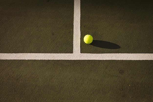 Vista ad alto angolo della pallina da tennis gialla da linee bianche al campo da tennis durante il tramonto, copia spazio