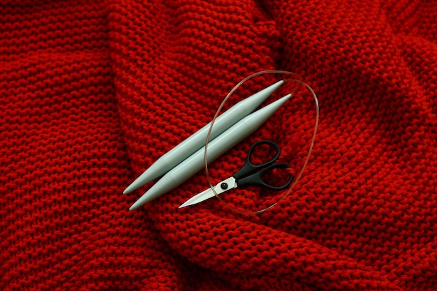 Vista ad alto angolo di aghi e forbici su una coperta a maglia rossa