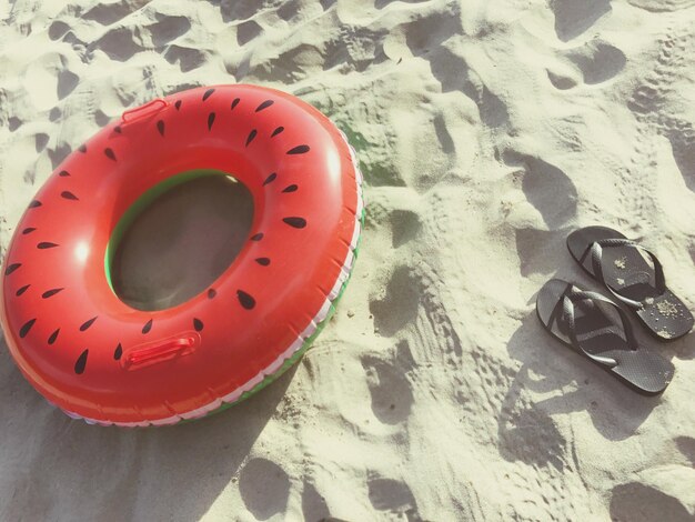 Vista ad alto angolo di anello gonfiabile e pantofole a spiaggia sabbiosa