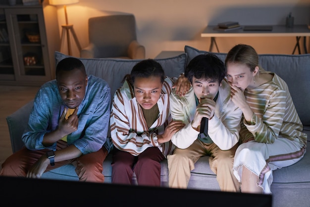 Vista ad alto angolo di diversi gruppi di amici che guardano la TV a casa illuminata da una luce blu