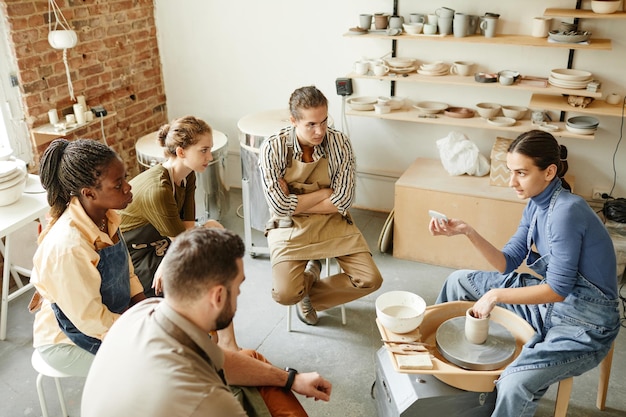 Vista ad alto angolo di diversi gruppi di persone al laboratorio di ceramica in uno studio accogliente, spazio copia