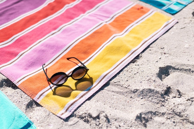 Vista ad alto angolo di occhiali da sole e asciugamano colorato sulla spiaggia sabbiosa durante la giornata di sole. Copia spazio, inalterato, protezione, vacanza, moda, picnic e concetto estivo.