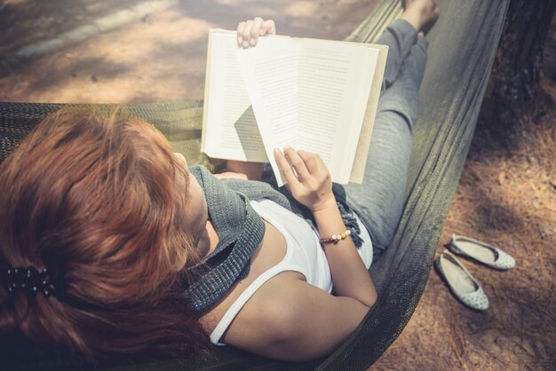 Vista ad alto angolo di una donna che legge un libro mentre è seduta in una amaca