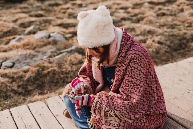 Vista ad alto angolo di una donna che usa il telefono cellulare mentre è seduta sul sentiero durante l'inverno