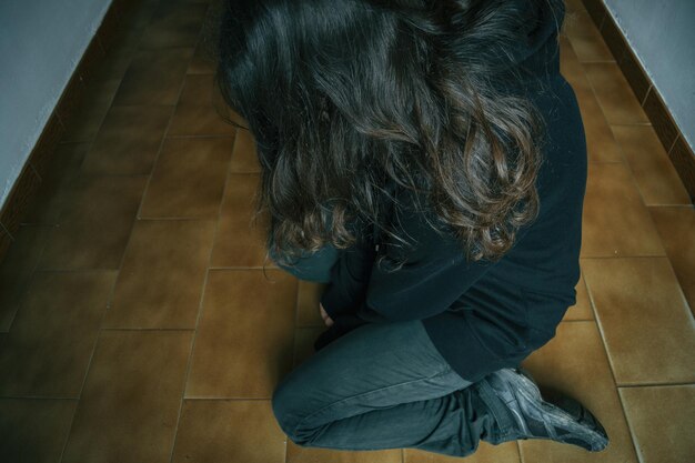 Vista ad alto angolo di una donna depressa inginocchiata sul pavimento di piastrelle