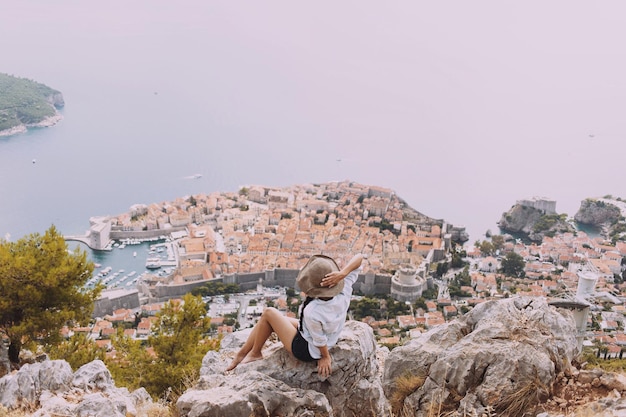 Vista ad alto angolo di una donna seduta su una roccia contro la città vecchia dal mare