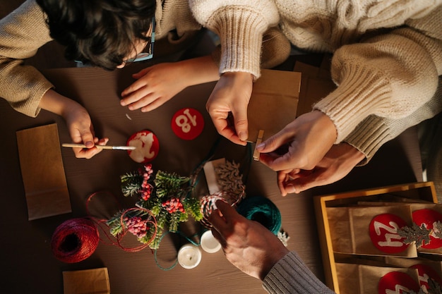 Vista ad alto angolo di una famiglia irriconoscibile che fa il calendario dell'avvento di Natale insieme seduti a tavola in casa alla vigilia di Natale