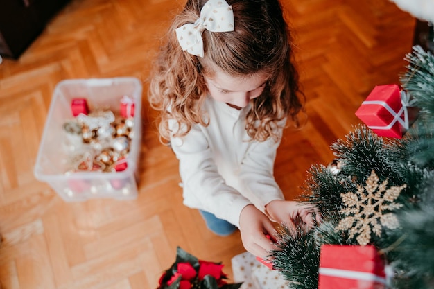 Vista ad alto angolo di una ragazza carina che decora l'albero di Natale a casa