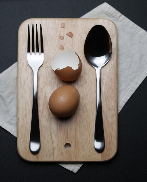 Vista ad alto angolo di uova marroni bollite per guscio d'uovo in mezzo a stoviglie su vassoio di legno