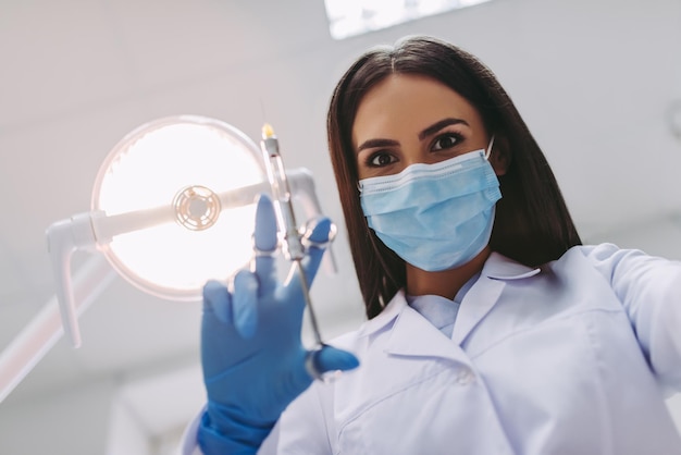 Vista ad angolo basso del dentista in maschera medica che tiene la siringa nella moderna clinica dentale