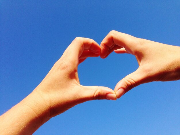 Vista ad angolo basso della mano che fa la forma di un cuore contro un cielo blu limpido