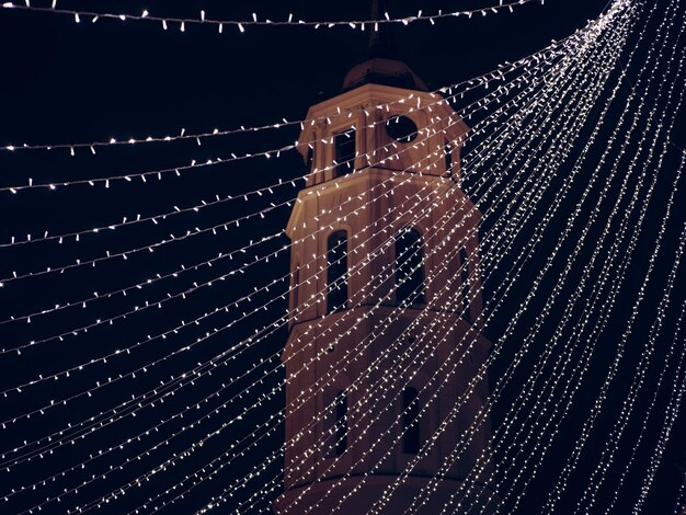 Vista ad angolo basso delle luci a corda illuminate contro la chiesa di notte