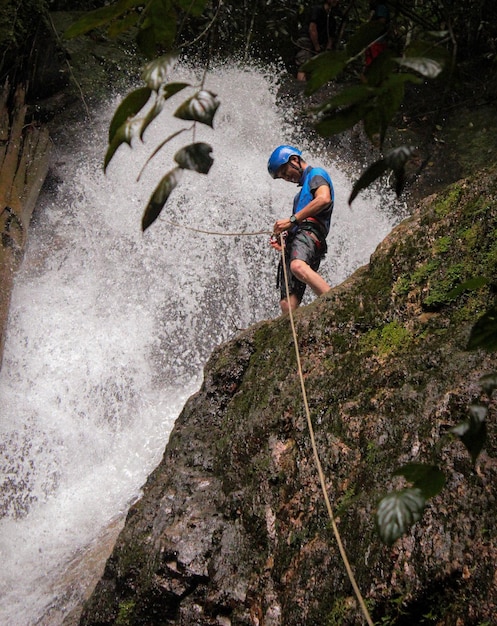 Vista ad angolo basso di un uomo che lega una corda mentre si trova sulla scogliera contro la cascata