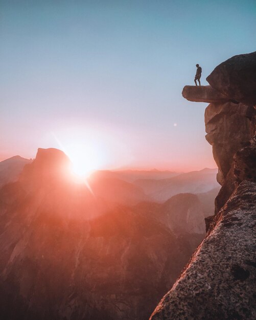 Vista ad angolo basso di un uomo in piedi su una scogliera contro il cielo durante il tramonto