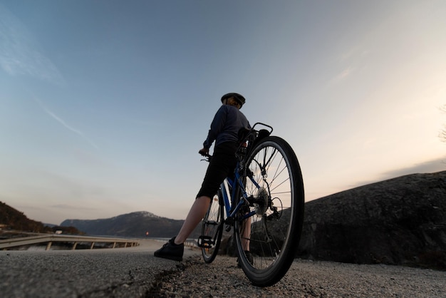 Vista ad angolo basso di un uomo maturo in bicicletta sulla strada contro il cielo durante il tramonto