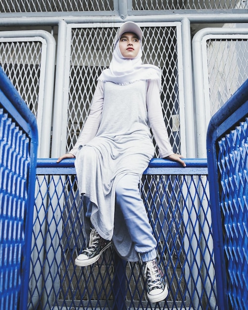 Vista ad angolo basso di una donna che indossa l'hijab seduta sulla ringhiera
