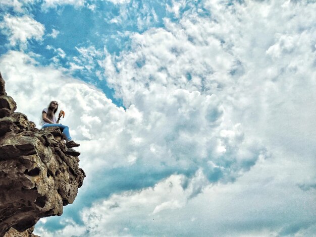 Vista ad angolo basso di una donna seduta su una formazione rocciosa contro un cielo nuvoloso