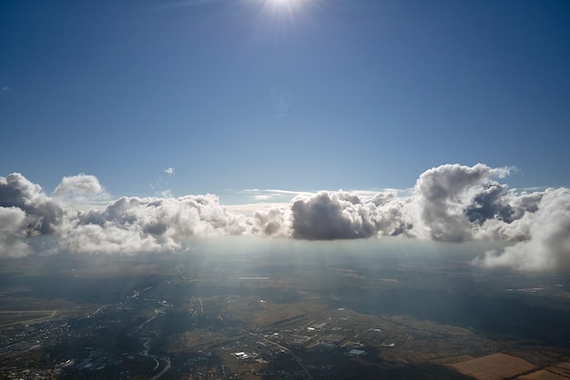 Vista aerea dal finestrino dell'aeroplano ad alta quota della città lontana ricoperta di nubi cumuliformi bianche e gonfie