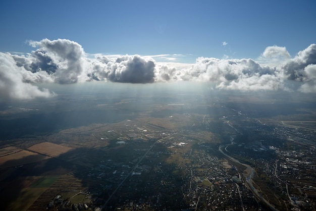 Vista aerea dal finestrino dell'aeroplano ad alta quota della città lontana ricoperta di nubi cumuliformi gonfie che si formano prima del temporale