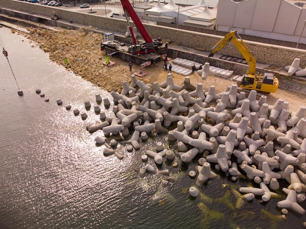 Vista aerea dall'alto della costruzione del frangiflutti Bulldozer e gru su un mucchio di massi nel mare