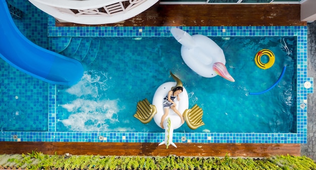 Vista aerea dall'alto della piscina con una donna che si rilassa giocando su un materasso gonfiabile in piscina