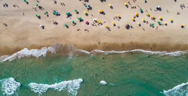 Vista aerea dall'alto delle onde che si infrangono sulla riva. Ombrelloni colorati e persone che si godono l'estate. Spiaggia brasiliana.