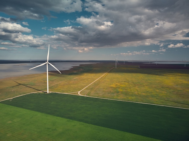 Vista aerea dall'alto delle turbine eoliche e del campo agricolo vicino al mare al tramonto