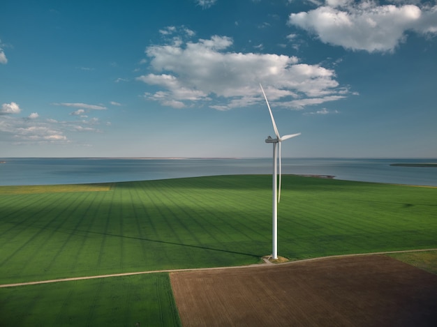 Vista aerea dall'alto delle turbine eoliche e del campo agricolo vicino al mare al tramonto