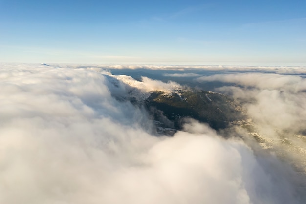 Vista aerea dall'alto di nuvole gonfie bianche che coprono le cime delle montagne innevate in una luminosa giornata di sole.